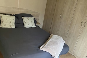 A bedroom with a bed, pillows, a blanket, and a wardrobe. - Caravan - Sleeps 6 - Parking, Pool, Facilities (Colchester)