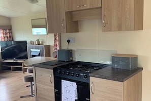A compact kitchen with a gas stove, a toaster, and wooden cabinets. - Caravan - Sleeps 6 - Parking, Pool, Facilities (Colchester)