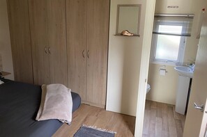 Makuuhuone, jossa on sänky, puinen vaatekaappi sekä kylpyhuone, jossa on pesuallas ja peili.