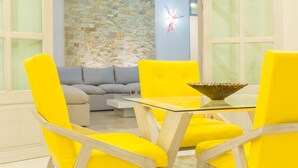 A room with a stone wall, a sofa, and bright yellow chairs around a glass table with a decorative bowl. - Mansion Serenity en Puerto Aventuras (Puerto Aventuras)