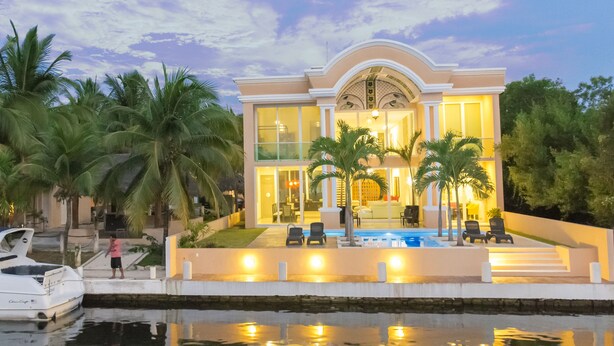 A modern house with a pool, palm trees, and a boat docked by the water. - Mansion Serenity en Puerto Aventuras (Puerto Aventuras)