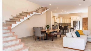 A spacious living area with a staircase, a dining table with chairs, a sofa, and a kitchen in the background. - Villa Sol By Desert Villas (Cabo San Lucas)