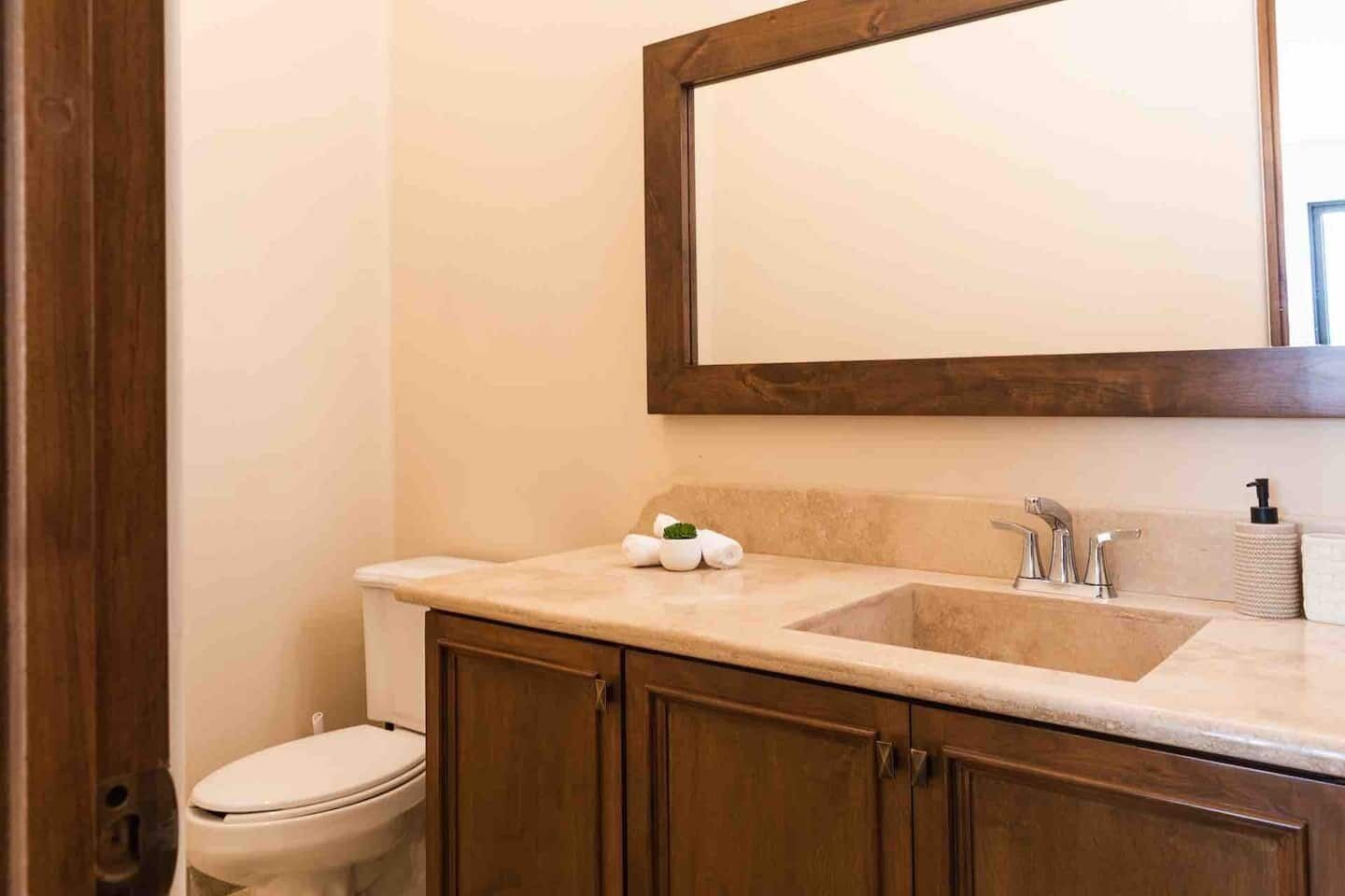 A bathroom with a wooden vanity, a sink with two faucets, and a toilet.