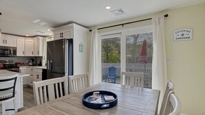 Una cocina moderna con armarios blancos, un refrigerador de acero inoxidable y un comedor con una mesa y sillas de madera.