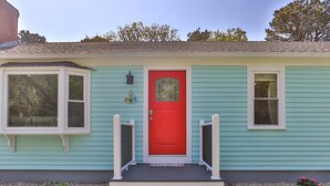 Una casa con puerta principal roja, ventanal saliente y un porche pequeño con escalones.