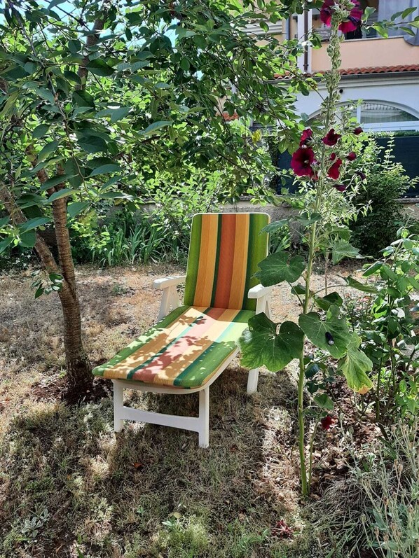Un jardin avec une chaise blanche dotée d’un dossier et d’un coussin d’assise à rayures colorées.