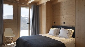 A wooden cabin bedroom with a bed, a chair, and a view of snow-capped mountains through a window. - Bishorn COSY chalet 4 personnes (Les Masses)