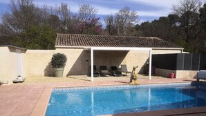 A swimming pool with a tiled deck, a covered patio area with lounge chairs, and a stone sculpture. - Maisonnette with swimming pool access, on the campsite (Aix en Provence)