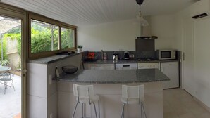 A modern kitchen with a large island, white cabinets, and a view of greenery through the window. - Maisonnette with swimming pool access, on the campsite (Aix en Provence)