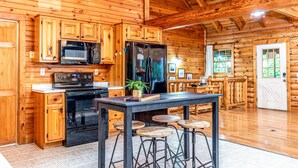 Cocina de cabaña de troncos con armarios de madera, estufa negra, refrigerador y una zona de bar con taburetes.