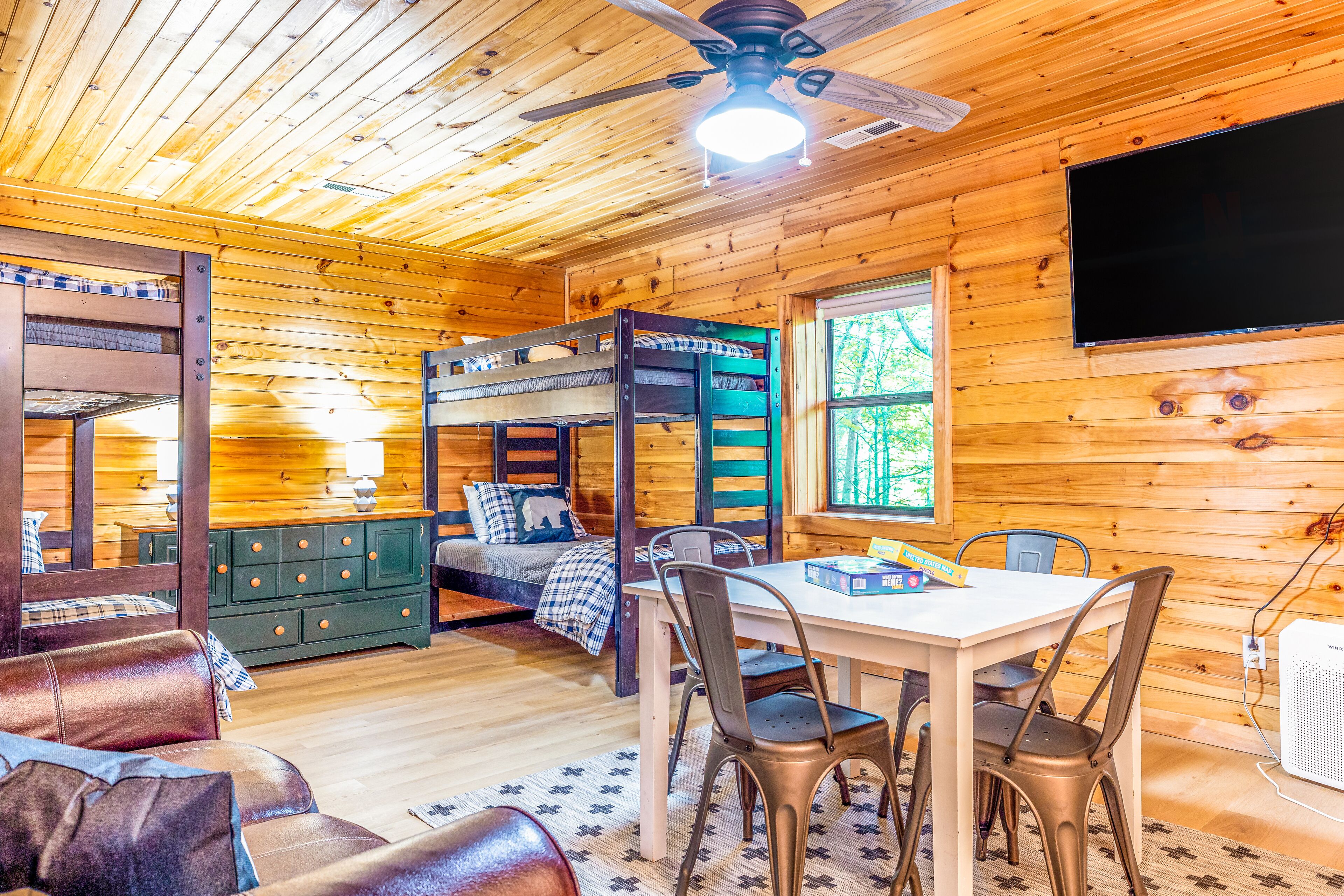 Ein Ferienhaus-Innenraum mit Etagenbett, Holzwänden, einem Esstisch mit Stühlen und einem Deckenventilator.