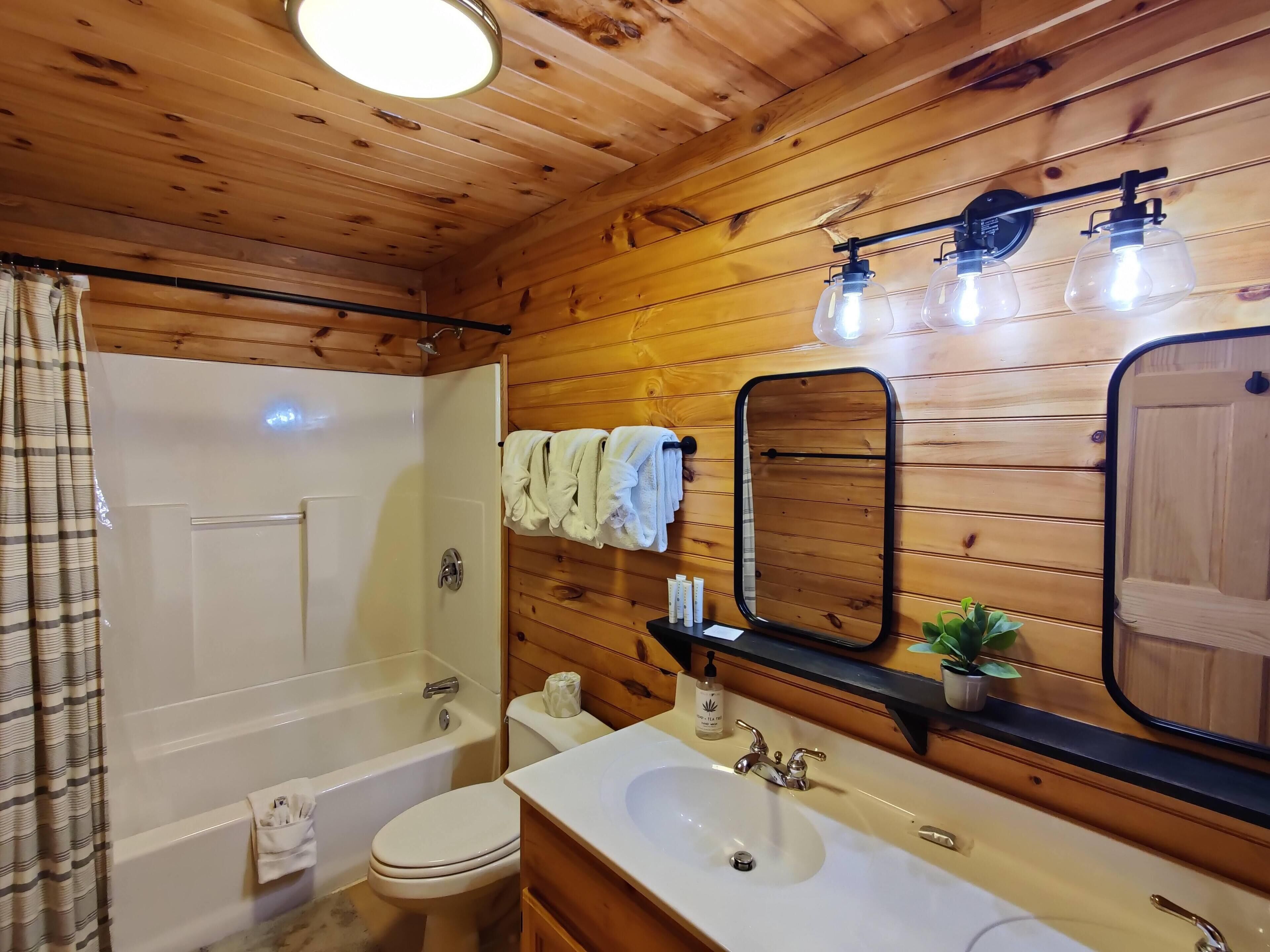 Une salle de bain aux murs lambrissés, équipée d’une baignoire, de toilettes, d’un lavabo et d’un miroir.