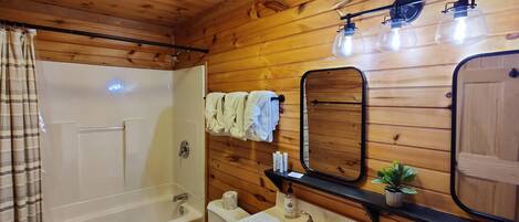Une salle de bain aux murs lambrissés, équipée d’une baignoire, de toilettes, d’un lavabo et d’un miroir.