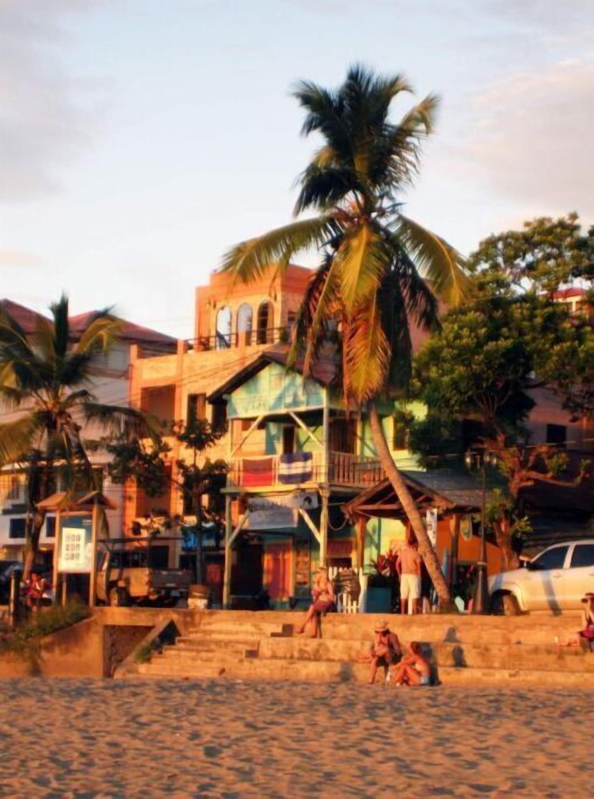 A beachfront property with a staircase leading to a building, palm trees, and a sandy beach.