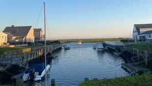 A marina with boats docked, a sailboat in the distance, and houses on the shore.