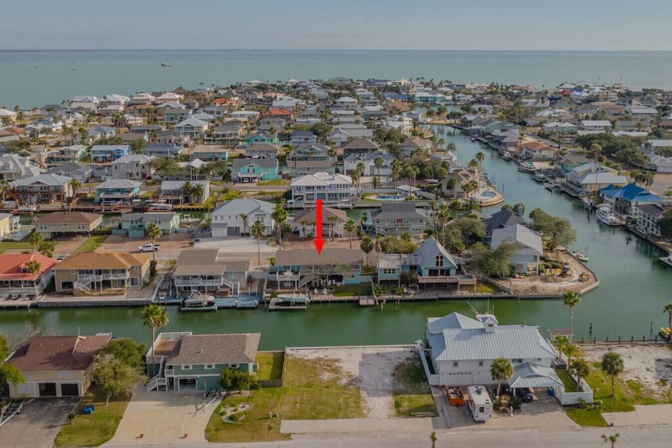 An aerial view of a coastal residential area with houses, a marina, and a large body of water.