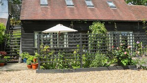 A rustic wooden building with a sloped roof, a wooden fence, and potted plants. - The Barn at Sandhole Cottage (Tonbridge)