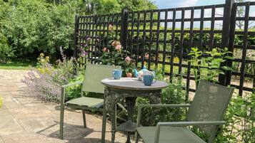 Een terras buiten met een ronde tafel en twee stoelen, omgeven door een tuin met verschillende planten en bloemen.