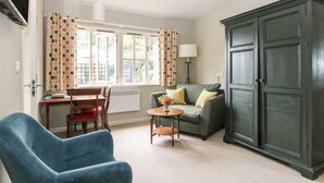 A living room with a blue armchair, a green sofa, a wooden table with a vase of flowers, and a dark green wardrobe. - The Barn at Sandhole Cottage (Tonbridge)