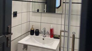 Et moderne badeværelse med en hvid vask, et spejl og en bruseniche.