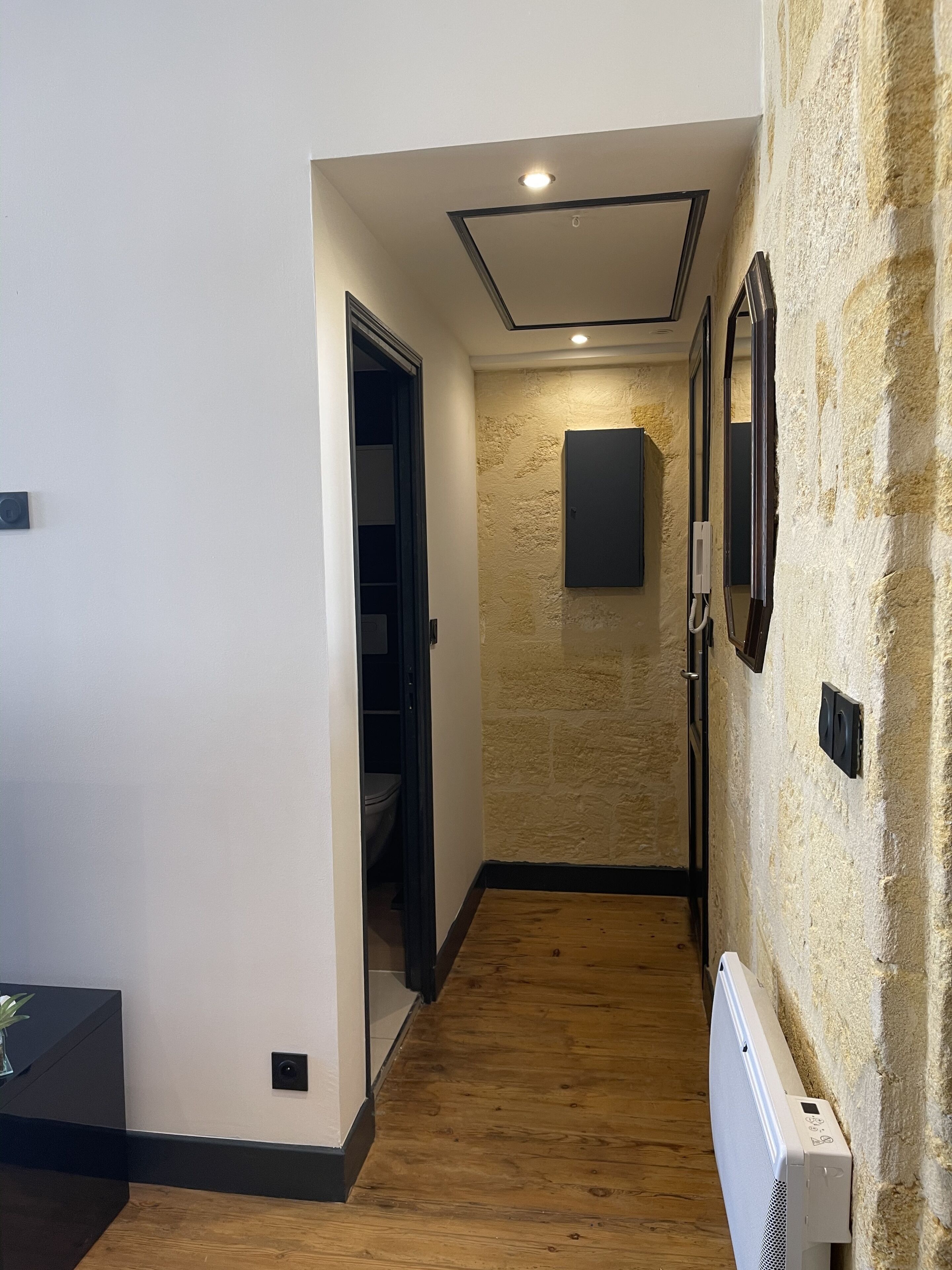 A hallway with a wooden floor, a stone wall, and a door leading to a bathroom.
