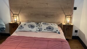 En seng med et trægavl, to sengeborde med lamper, mønstrede puder og et rosa sengetæppe.