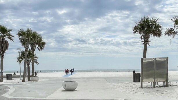 Ein Strand mit Palmen, einem Betonweg und einigen Spaziergängern.