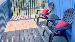 Eine Holzterrasse mit zwei Stühlen und einem Tisch, mit Blick auf einen Parkplatz und Gebäude.