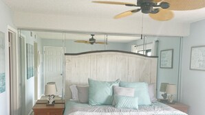 Ein Schlafzimmer mit einem Bett, einem Nachttisch, einem Deckenventilator und einer Tür zu einem anderen Raum.