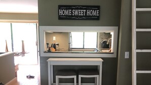 Eine Küchenzeile mit einem 'HOME SWEET HOME'-Schild, Holzboden und einer weißen Arbeitsplatte mit Sitzgelegenheiten.