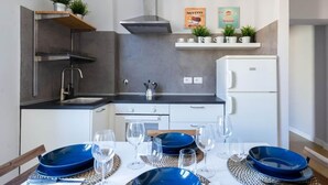 A modern kitchen with a built-in stove, a sink, and a white refrigerator. There are two shelves above the counter with decorative items and plants. - Two Bedroom Apartment (roma)