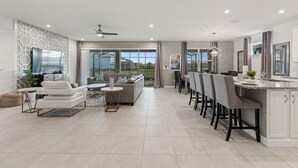 A spacious living area with a modern kitchen, a dining area, and a large window providing a view of the outdoors. - Lake Views, Private Pool, Spa and Premium Resort Amenities Included! (Kissimmee)
