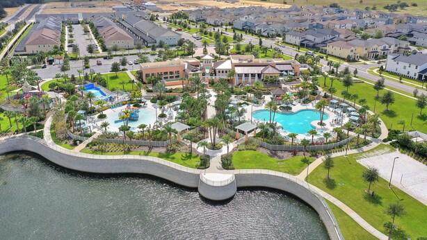 A residential area with a large swimming pool surrounded by houses and a bridge over a body of water. - Lake Views, Private Pool, Spa and Premium Resort Amenities Included! (Kissimmee)