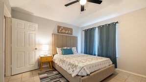 Un dormitorio con una cama, una mesita de noche, un ventilador de techo y una puerta.