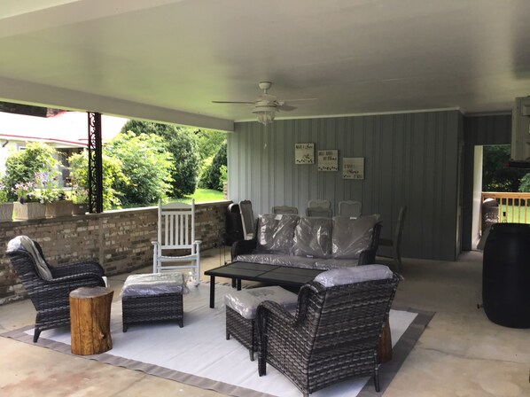 Ein überdachter Patio-Bereich mit Korbmöbeln, einem Deckenventilator und Blick auf einen Garten.