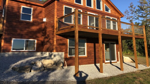 A two-story wooden house with a balcony, large windows, and a gravel driveway. - Ski Retreat with scenic mountian and river views  (Hanover)