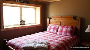 A bedroom with a wooden headboard, a checkered bedspread, and a window with a sign above it. - Ski Retreat with scenic mountian and river views  (Hanover)