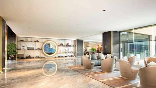 A modern lobby with a marble floor, seating area with sofas, a large circular mirror, and a wall with decorative items. - Wyndham Grand Royal Hotel Jinlin Lijiang (Lijiang)