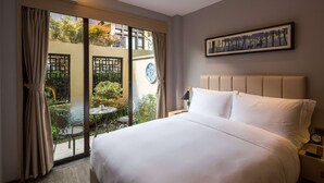 A hotel room with a large bed, a view of a garden through a sliding door, a framed artwork on the wall, and a nightstand with a lamp. - Wyndham Grand Royal Hotel Jinlin Lijiang (Lijiang)