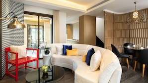 A modern living room with a curved sofa, a red chair, a round coffee table, and a dining area with a table and chairs. - Wyndham Grand Royal Hotel Jinlin Lijiang (Lijiang)