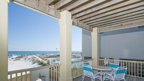 Eine überdachte Terrasse mit Blick auf den Strand, einen Pool und einen Tisch mit Stühlen.