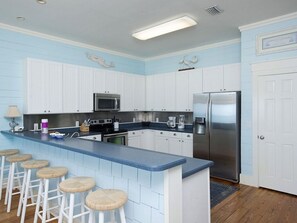 A kitchen with white cabinets, a blue countertop, stainless steel appliances, and bar stools.