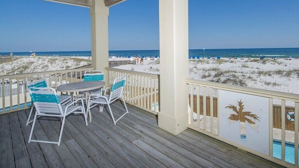 Eine überdachte Terrasse mit Tisch und Stühlen, mit Blick auf einen Strand mit Dünen und dem Meer.