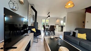 Un salon moderne avec un téléviseur à écran plat, un canapé, un coin repas et une cuisine en arrière-plan.