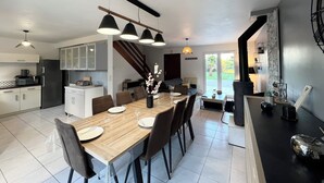 Une cuisine moderne avec un coin repas, comprenant une table en bois dressée pour six personnes, un escalier menant à une mezzanine et une vue sur l’extérieur.