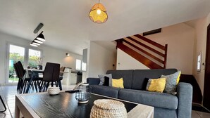 Un salon moderne avec un canapé gris, une table basse en bois et un coin repas comprenant des chaises et une table.