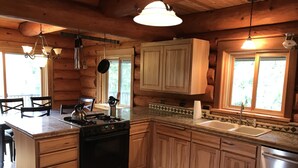 A log cabin kitchen with wooden cabinets, a stove, a sink, and a dining area with chairs. - 6 BDRM Log Cabin on Big Fall Creek (Fall Creek)