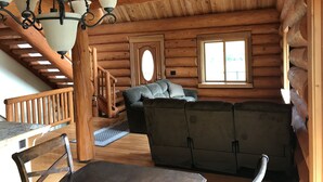 A log cabin interior with a wooden staircase, a sofa, and a dining area. - 6 BDRM Log Cabin on Big Fall Creek (Fall Creek)