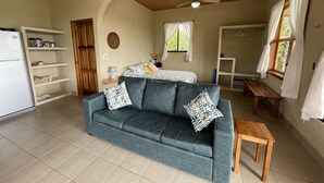 Een woonkamer met een bank, een houten tafel, een plafondventilator en een raam met gordijnen.
