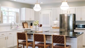 A kitchen with white cabinets, a stainless steel refrigerator, a microwave, and a dining area with a central island and chairs. - Cozy cottage, just a short walk to UofA (Fayetteville)